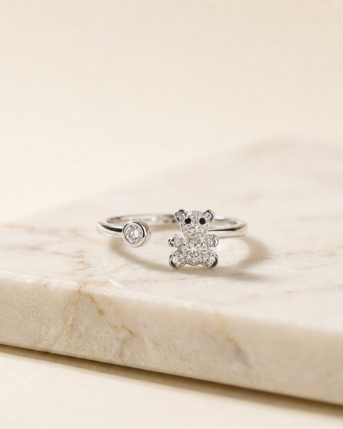 Anillo Oso Regulable de plata 925 abierto, con osito de circonitas y una piedra en el otro extremo, sobre mármol