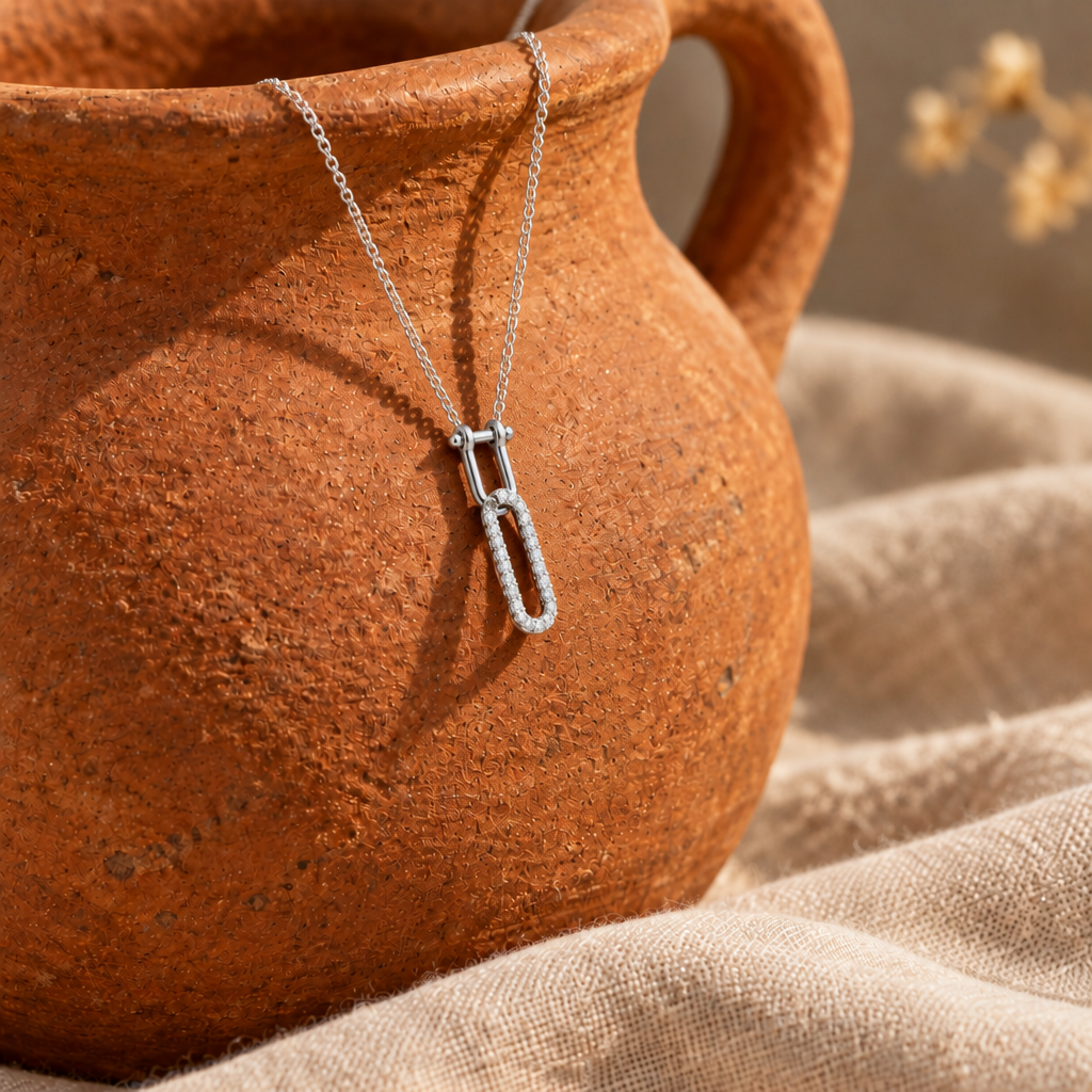 Collar de plata 925 con dije de dos eslabones, uno liso y uno con piedras, colgado de una jarra de barro